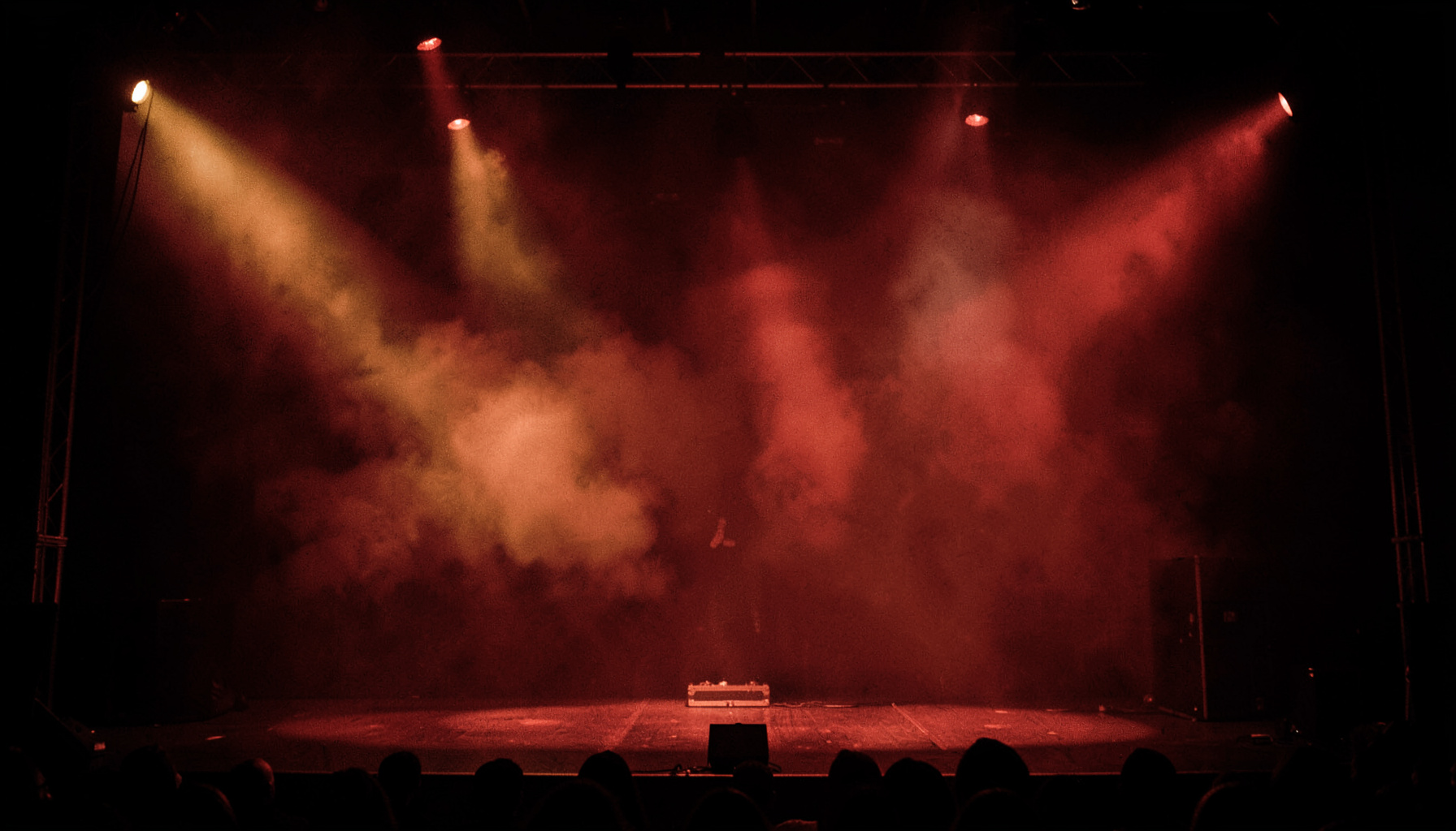 A dark concert stage with warm amber and red stage lights cutting through haze, creating a dramatic atmospheric glow